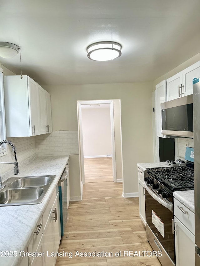 218 S Hayford Ave, Lansing, MI 48912 - kitchen with appliances with stainless steel finishes, a sink, light wood-style floors, decorative backsplash, and white cabinetry