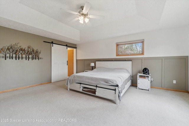 549 Riverwalk Dr, Mason, MI 48854 - carpeted bedroom featuring a decorative wall, a barn door, a tray ceiling, wainscoting, and a ceiling fan