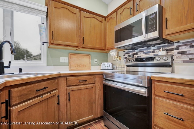 722 Fieldview Dr, Grand Ledge, MI 48837 - kitchen featuring stainless steel appliances, light countertops, a sink, and brown cabinetry