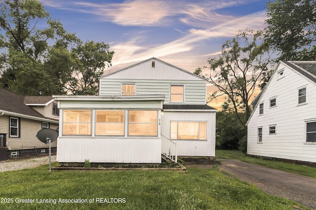 316 S Rosemary Ave, Lansing, MI 48917 - back of property at dusk with a sunroom, a yard, and a shingled roof