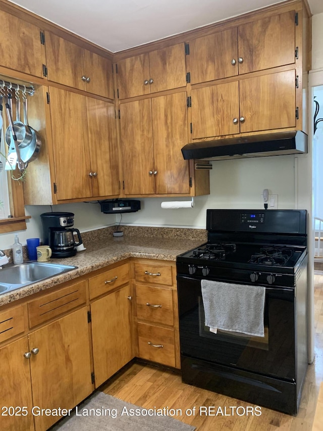 575 Brookland Blvd, Lansing, MI 48910 - kitchen featuring black range with gas stovetop, under cabinet range hood, light wood-style floors, a sink, and brown cabinetry