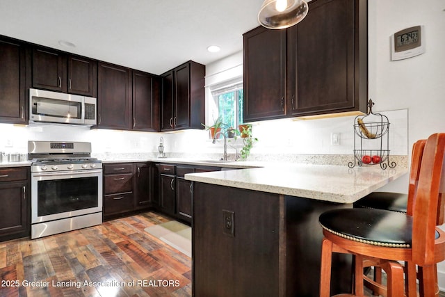 4269 Tamarack St, Holt, MI 48842 - kitchen with stainless steel appliances, a sink, a peninsula, dark brown cabinetry, and recessed lighting