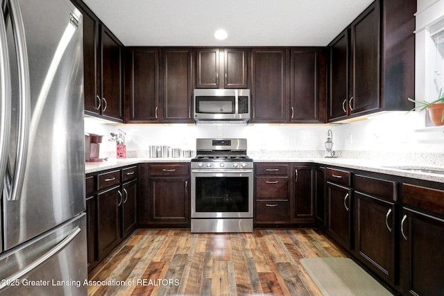 4269 Tamarack St, Holt, MI 48842 - kitchen with appliances with stainless steel finishes, wood finished floors, dark brown cabinets, light stone counters, and recessed lighting