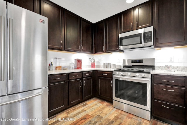 4269 Tamarack St, Holt, MI 48842 - kitchen with appliances with stainless steel finishes, light wood finished floors, dark brown cabinets, and light stone counters