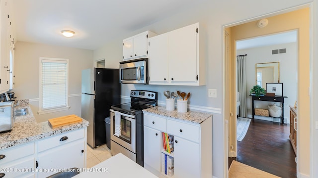 1451 Harvard Rd, East Lansing, MI 48823 - kitchen featuring appliances with stainless steel finishes, white cabinets, light stone counters, and light wood-style floors