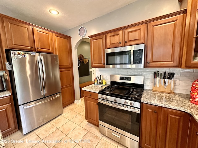 11195 W Herbison Rd, Eagle, MI 48822 - kitchen featuring appliances with stainless steel finishes, arched walkways, brown cabinets, backsplash, and a textured ceiling