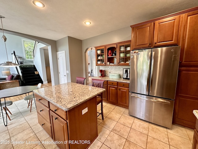 11195 W Herbison Rd, Eagle, MI 48822 - kitchen featuring freestanding refrigerator, arched walkways, glass insert cabinets, decorative backsplash, and a center island