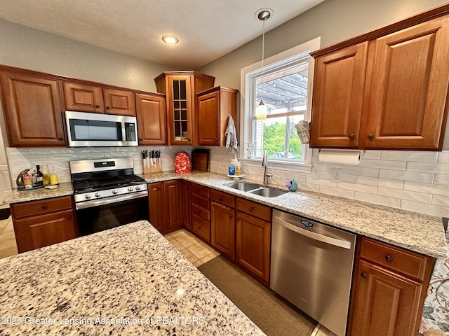 11195 W Herbison Rd, Eagle, MI 48822 - kitchen featuring stainless steel appliances, a sink, light stone counters, brown cabinetry, and decorative backsplash