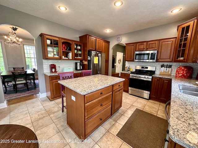 11195 W Herbison Rd, Eagle, MI 48822 - kitchen with appliances with stainless steel finishes, arched walkways, a chandelier, tasteful backsplash, and a kitchen island