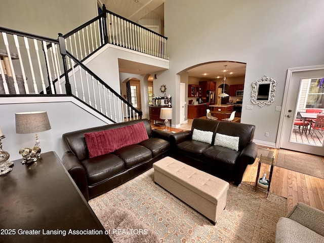 11195 W Herbison Rd, Eagle, MI 48822 - living room with arched walkways, a high ceiling, wood finished floors, stairs, and baseboards