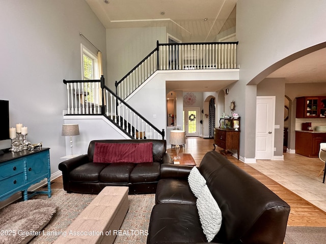 11195 W Herbison Rd, Eagle, MI 48822 - living room with arched walkways, a towering ceiling, stairs, wood finished floors, and baseboards