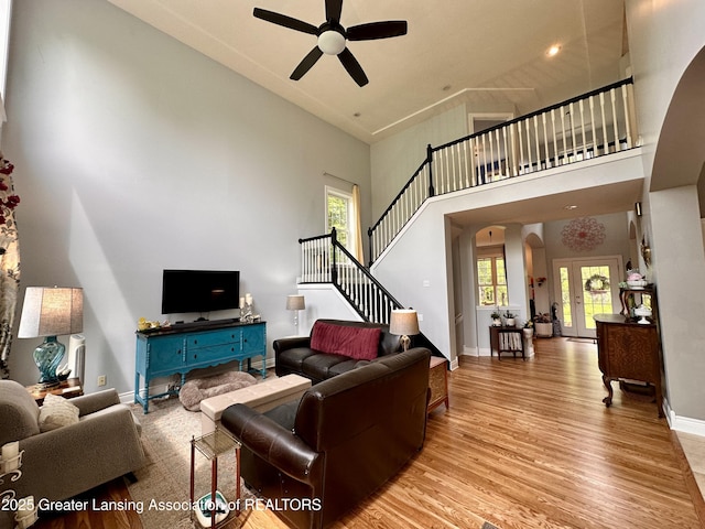 11195 W Herbison Rd, Eagle, MI 48822 - living area with a towering ceiling, arched walkways, a ceiling fan, light wood-type flooring, and stairs