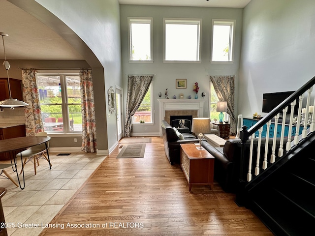 11195 W Herbison Rd, Eagle, MI 48822 - living room featuring arched walkways, a towering ceiling, light wood finished floors, a glass covered fireplace, and baseboards
