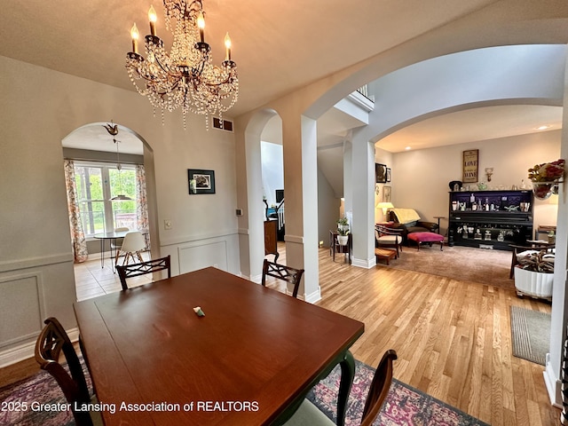 11195 W Herbison Rd, Eagle, MI 48822 - dining room with arched walkways, a chandelier, light wood-type flooring, a wainscoted wall, and a decorative wall