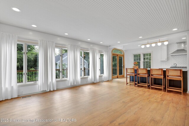 350 Kensington Rd, East Lansing, MI 48823 - kitchen with wall chimney range hood, light wood-type flooring, recessed lighting, decorative backsplash, and a breakfast bar