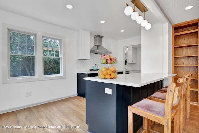 350 Kensington Rd, East Lansing, MI 48823 - kitchen with wall chimney range hood, light wood finished floors, backsplash, a kitchen bar, and light countertops