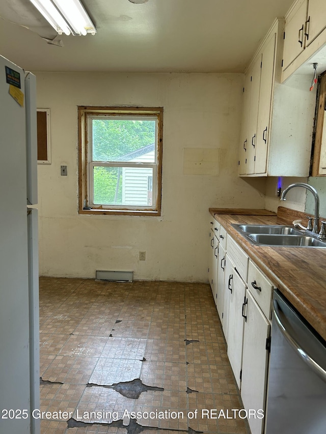 657 Spartan Ave, East Lansing, MI 48823 - kitchen featuring stainless steel dishwasher, a sink, freestanding refrigerator, white cabinetry, and brick patterned flooring