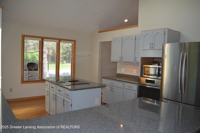 2397 Emerald Forest Cir Unit 26, East Lansing, MI 48823 - kitchen with appliances with stainless steel finishes, light wood-type flooring, decorative backsplash, a kitchen island, and dark stone counters