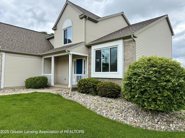 1512 Lindy Dr, Lansing, MI 48917 - traditional-style home featuring covered porch, a front yard, roof with shingles, and brick siding