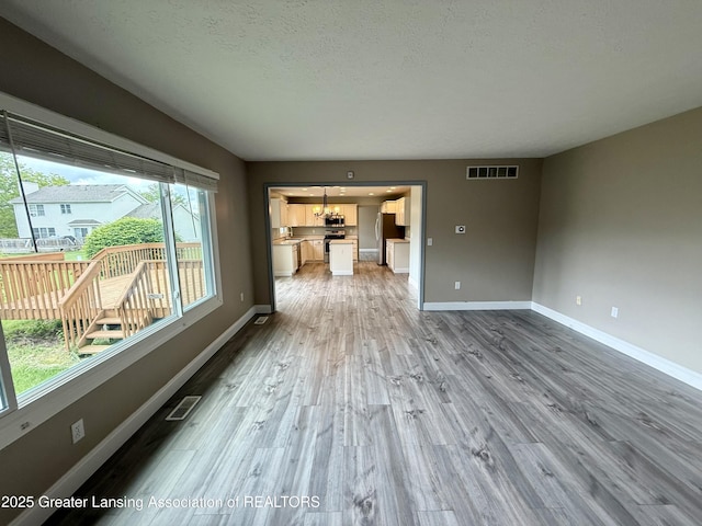1512 Lindy Dr, Lansing, MI 48917 - unfurnished living room featuring wood finished floors, baseboards, a textured ceiling, and a chandelier
