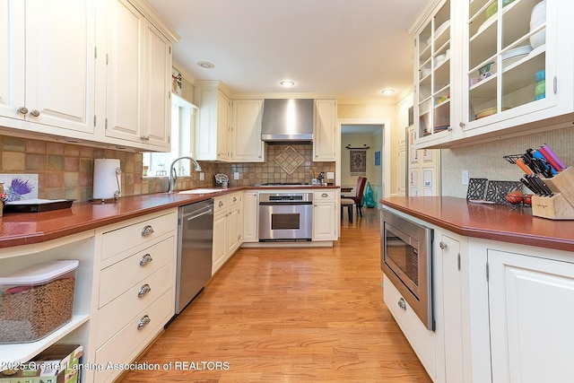 4767 Mohican Ln, Okemos, MI 48864 - kitchen with stainless steel appliances, a sink, wall chimney exhaust hood, light wood-style floors, and glass insert cabinets