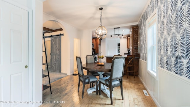 9181 Coleman Rd, Haslett, MI 48840 - dining space featuring a barn door, light wood-style flooring, ornamental molding, arched walkways, and a chandelier