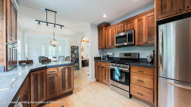 9181 Coleman Rd, Haslett, MI 48840 - kitchen with appliances with stainless steel finishes, dark countertops, rail lighting, arched walkways, and brown cabinetry