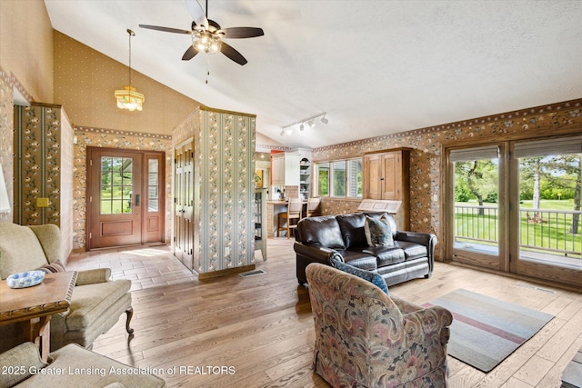 12560 Eaton Rapids Rd, Springport, MI 49284 - living room featuring wallpapered walls, lofted ceiling, healthy amount of natural light, light wood-style flooring, and a ceiling fan