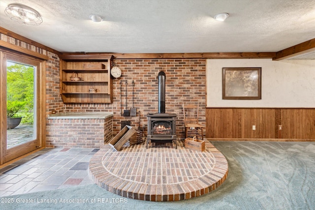 12560 Eaton Rapids Rd, Springport, MI 49284 - carpeted living area featuring a textured ceiling, a wood stove, wood walls, and a wainscoted wall