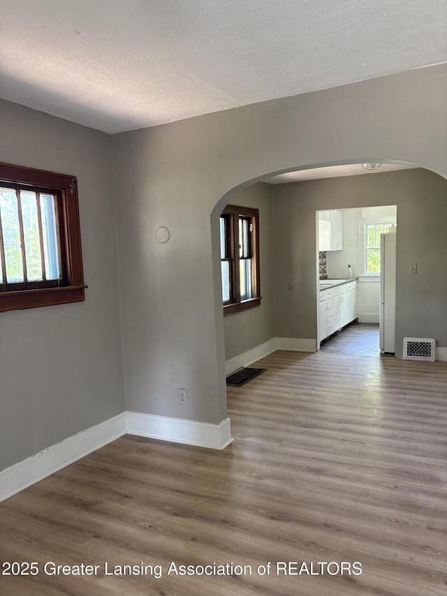 2113 S Rundle Ave, Lansing, MI 48910 - unfurnished room with arched walkways, wood finished floors, baseboards, and a textured ceiling