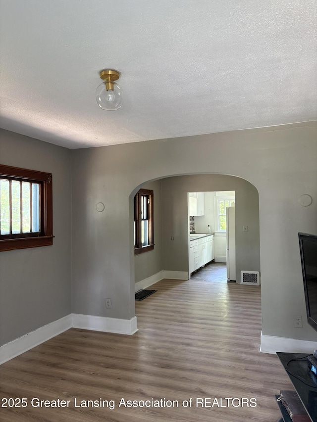 2113 S Rundle Ave, Lansing, MI 48910 - unfurnished living room with arched walkways, wood finished floors, baseboards, and a textured ceiling
