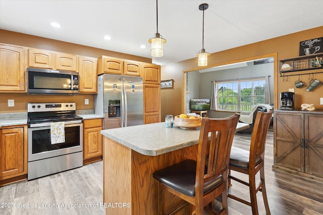 2424 S Canfield Rd, Eaton Rapids, MI 48827 - kitchen with stainless steel appliances, light wood-style flooring, light countertops, a breakfast bar, and hanging light fixtures