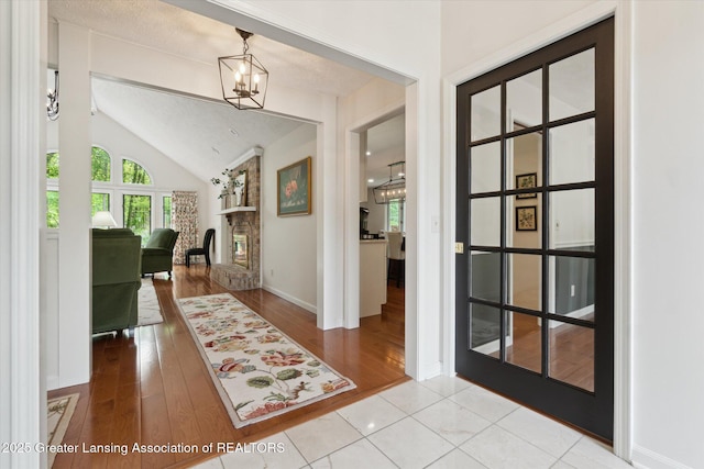 12728 Oneida Woods Trl, Grand Ledge, MI 48837 - foyer entrance featuring lofted ceiling, a fireplace, baseboards, wood finished floors, and a chandelier