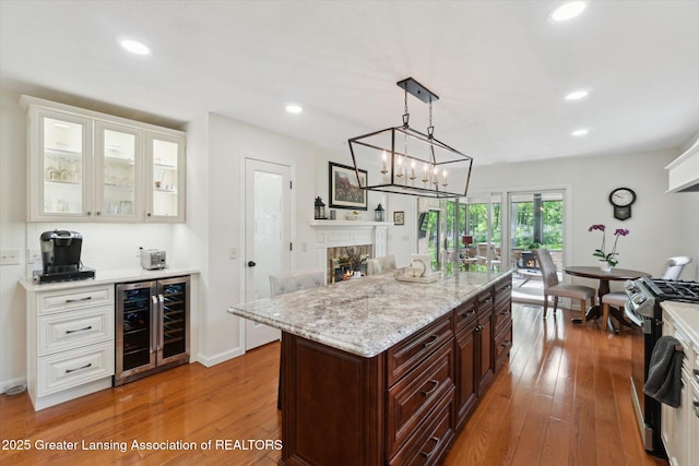 12728 Oneida Woods Trl, Grand Ledge, MI 48837 - kitchen featuring beverage cooler, gas stove, hardwood / wood-style flooring, white cabinets, and a glass covered fireplace