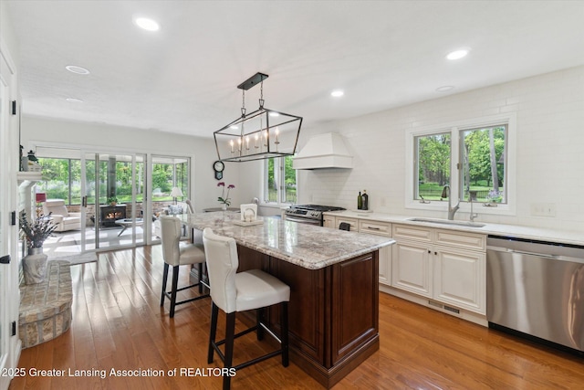 12728 Oneida Woods Trl, Grand Ledge, MI 48837 - kitchen with stainless steel appliances, custom exhaust hood, a sink, a breakfast bar, and light stone counters