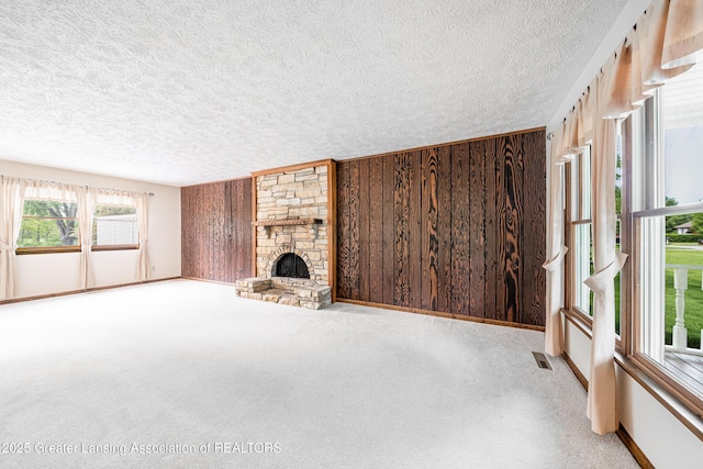 1932 Maple Shade Dr, Williamston, MI 48895 - unfurnished living room featuring a textured ceiling, carpet floors, wood walls, baseboards, and a stone fireplace