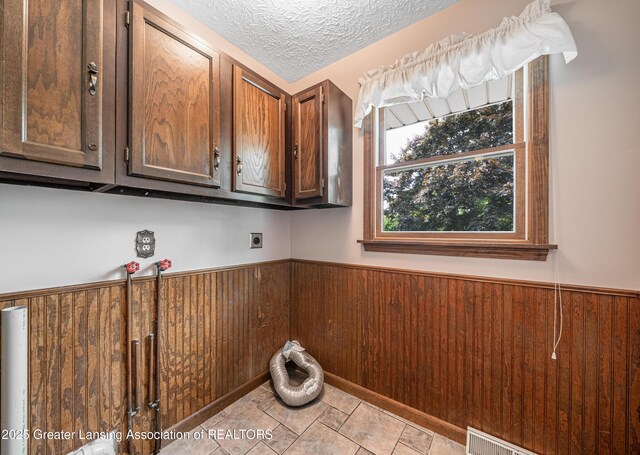 1932 Maple Shade Dr, Williamston, MI 48895 - laundry room featuring cabinet space, electric dryer hookup, a wainscoted wall, wooden walls, and a textured ceiling