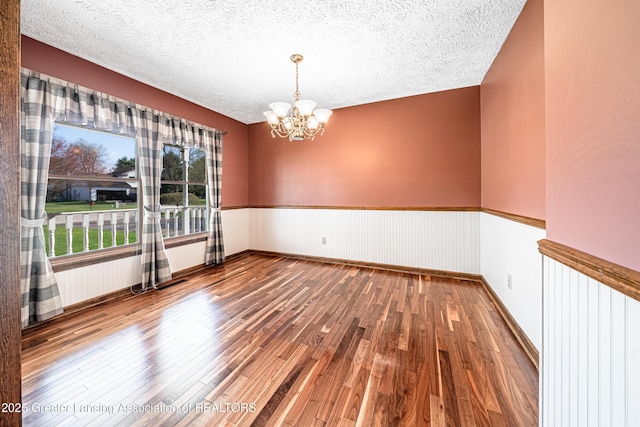 1932 Maple Shade Dr, Williamston, MI 48895 - unfurnished room with hardwood / wood-style floors, a chandelier, a wainscoted wall, and a textured ceiling