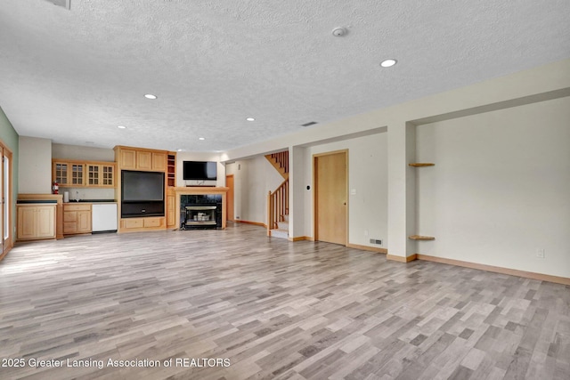 345 Linn Rd, Williamston, MI 48895 - unfurnished living room featuring light wood-style flooring, a textured ceiling, recessed lighting, a tiled fireplace, and stairway