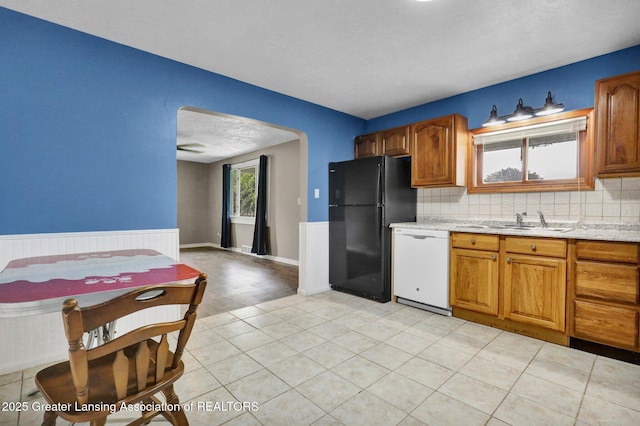 1246 House Rd N, Webberville, MI 48892 - kitchen with freestanding refrigerator, dishwasher, a sink, brown cabinets, and wainscoting