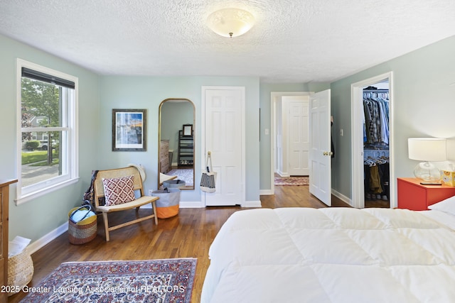 438 Bailey St, East Lansing, MI 48823 - bedroom with wood finished floors, a textured ceiling, baseboards, arched walkways, and a walk in closet