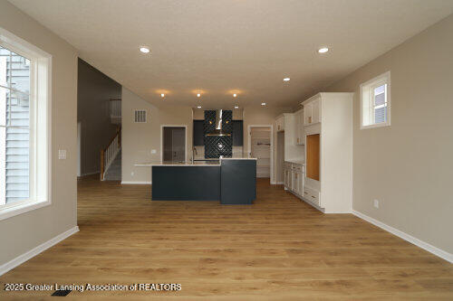 615 Magenta Ct, Haslett, MI 48840 - kitchen featuring wall chimney range hood, white cabinetry, a center island with sink, light wood finished floors, and baseboards