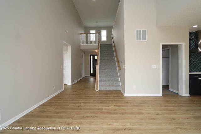 615 Magenta Ct, Haslett, MI 48840 - unfurnished living room featuring light wood-style flooring, stairs, a high ceiling, and baseboards