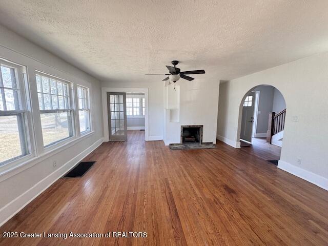 1305 W Hillsdale St, Lansing, MI 48915 - unfurnished living room with a textured ceiling, a fireplace with raised hearth, wood finished floors, arched walkways, and baseboards