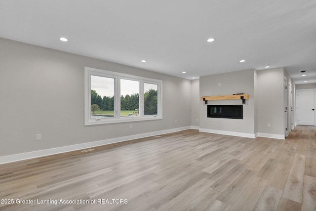 3115 Dietz Rd, Williamston, MI 48895 - unfurnished living room featuring light wood-style floors, recessed lighting, baseboards, and a glass covered fireplace