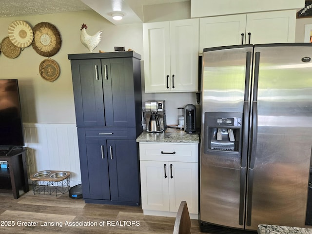 3066 S Canfield Rd, Eaton Rapids, MI 48827 - kitchen with stainless steel fridge with ice dispenser, wood finished floors, light stone counters, a wainscoted wall, and white cabinets