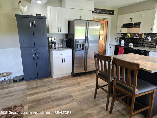 3066 S Canfield Rd, Eaton Rapids, MI 48827 - kitchen with stainless steel fridge with ice dispenser, black electric range, under cabinet range hood, white cabinetry, and a wainscoted wall