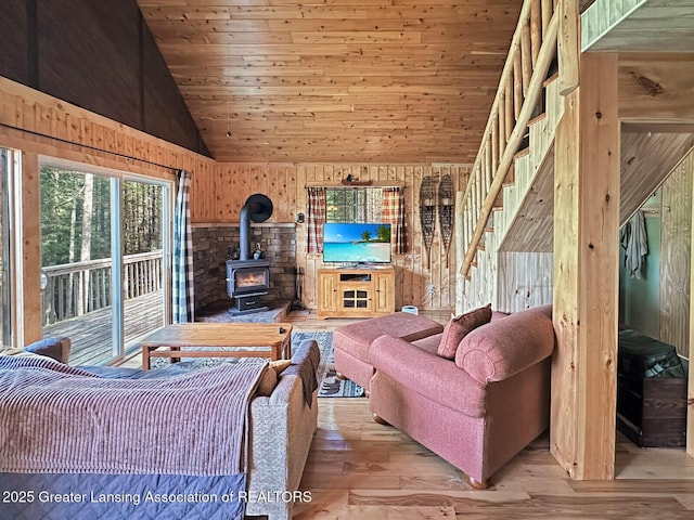 2623 Timberlane Trl, Grayling, MI 49738 - living area featuring a wood stove, vaulted ceiling, wooden walls, light wood-style flooring, and stairs