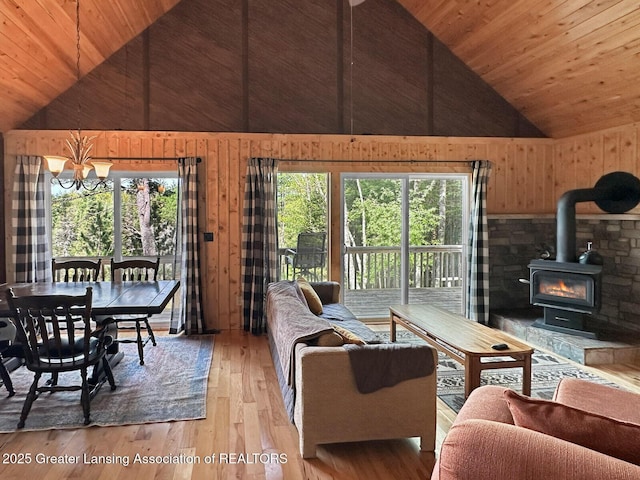 2623 Timberlane Trl, Grayling, MI 49738 - living room featuring a chandelier, wooden ceiling, a wood stove, wooden walls, and light wood-type flooring