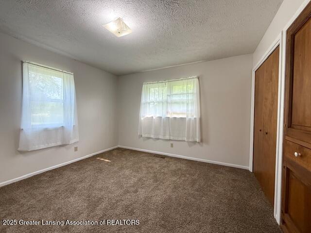 207 Wight St Unit 209, Elsie, MI 48831 - unfurnished bedroom with dark carpet, a textured ceiling, a closet, and baseboards